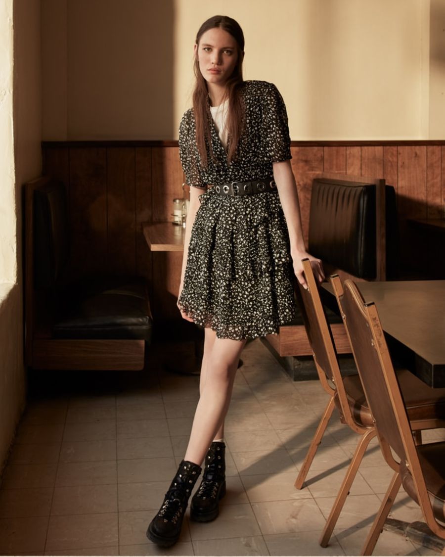 Imagen de una mujer de pie apoyada en una silla con un vestido de estampado floral en blanco y negro y unas botas de cuero.