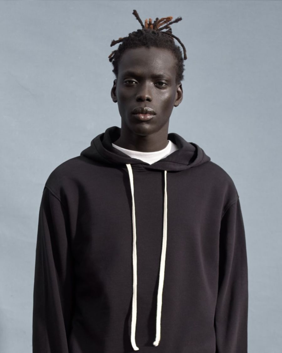 Portraitfoto von einem Mann, der einen schwarzen Kapuzenpullover über einem weißen T-Shirt trägt.