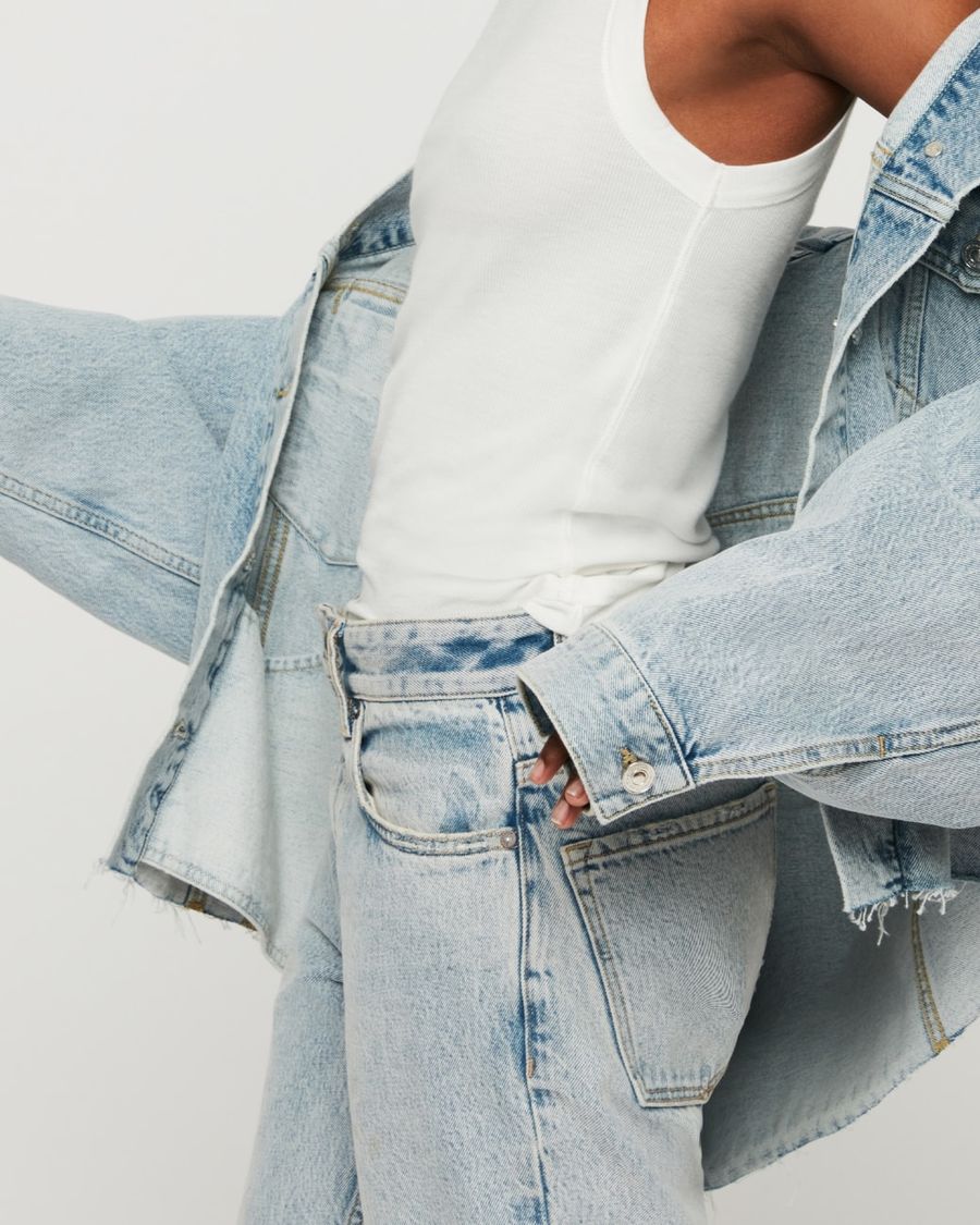 Image of a woman wearing a light denim jacket with a white tank and a light pair of jeans.