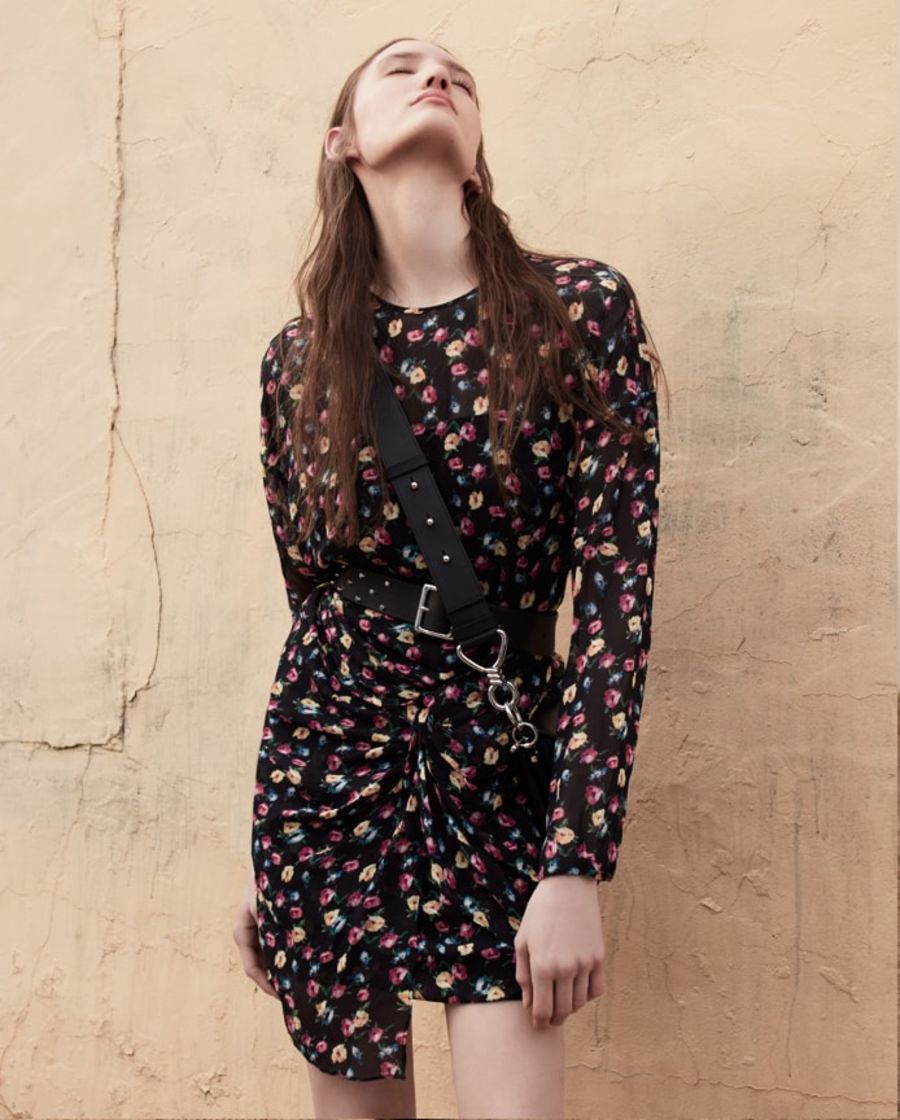 Image of a woman wearing a floral printed dress with a studded belt and a black crossbody bag.