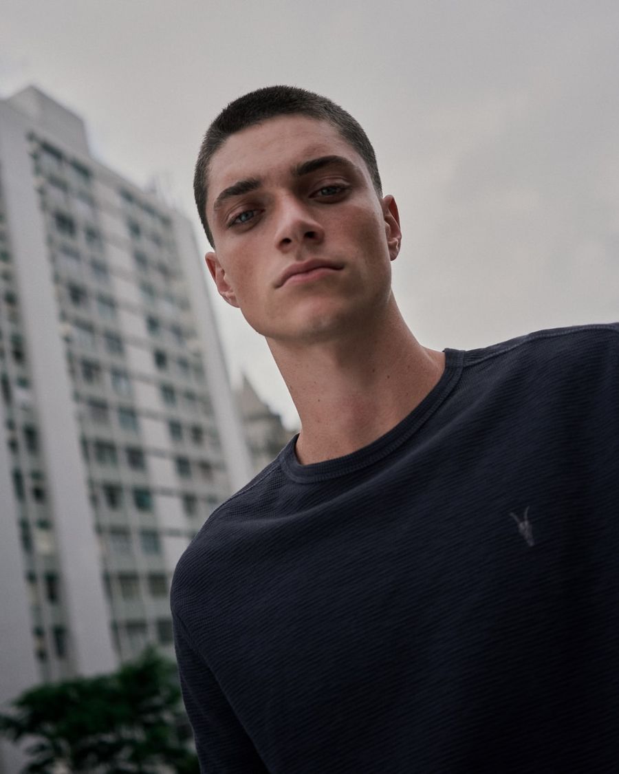Foto von einem Mann vor einem Gebäude, der ein dunkelblaues T-Shirt mit Ramskull-Logo trägt.