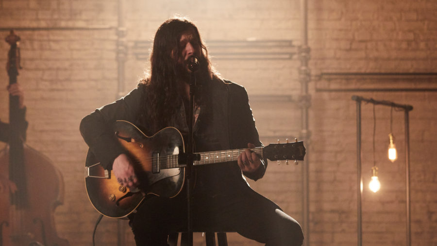 Shawn James tocando la guitarra durante la grabación de la última LA Sessions vistiendo una camisa vaquera con un blazer de piel negro y unos vaqueros negros.
