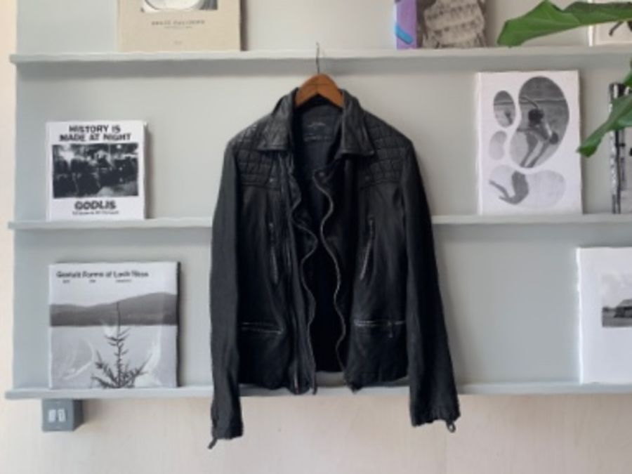 Image of a black leather jacket hanging from a shelf with books and magazines on.
