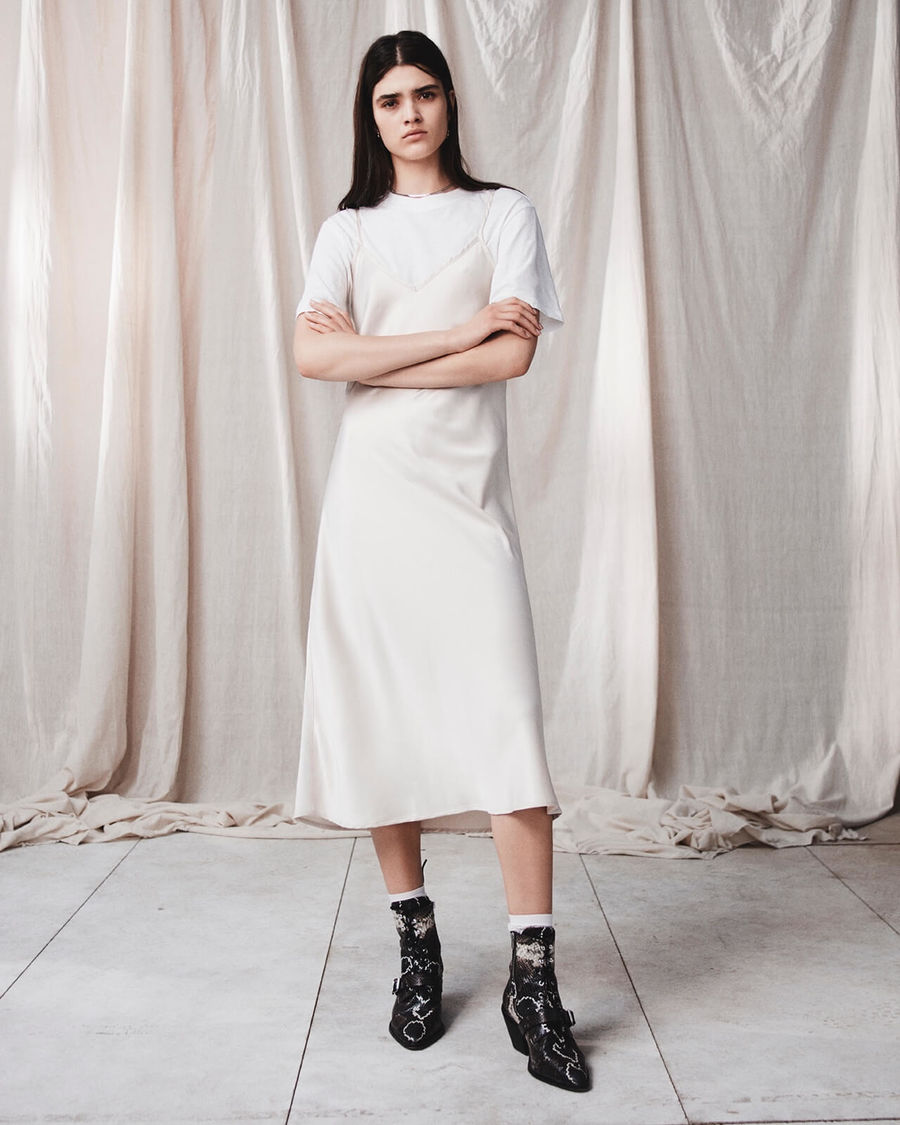 Image d'une femme portant une robe nuisette beige par dessus un t-shirt blanc avec des bottes imprimées serpent.