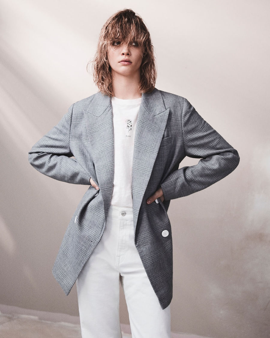 Portrait d'une femme portant un t-shirt blanc avec un jean blanc et un blazer à carreaux.