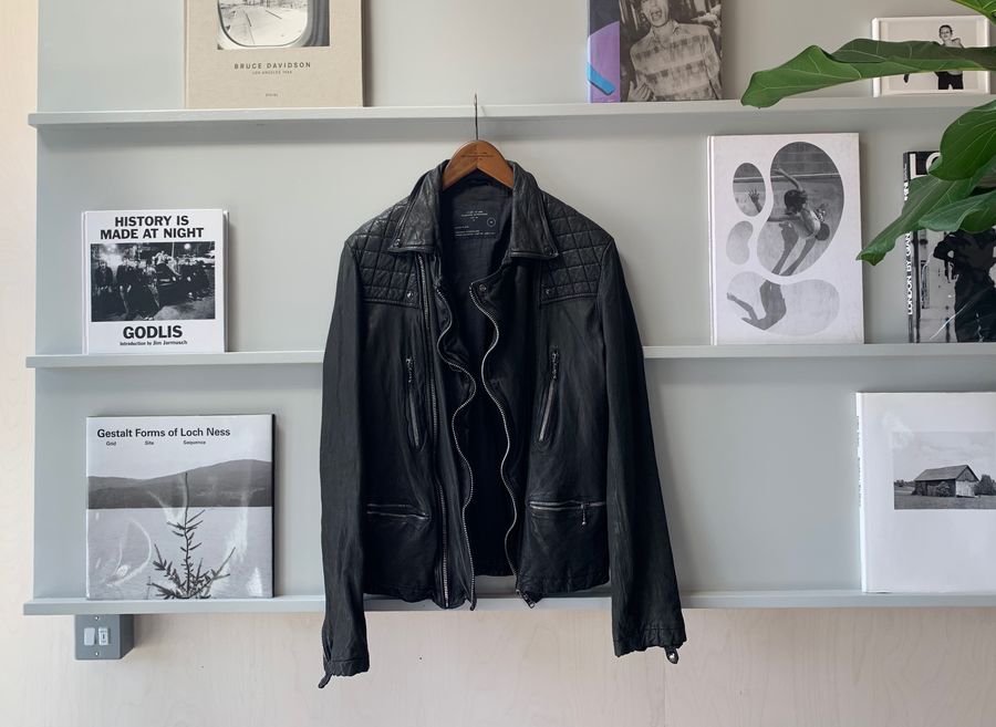 Foto von einer schwarzen Lederjacke, die auf einem Kleiderbügel an einem Regal mit Büchern und Magazinen hängt.