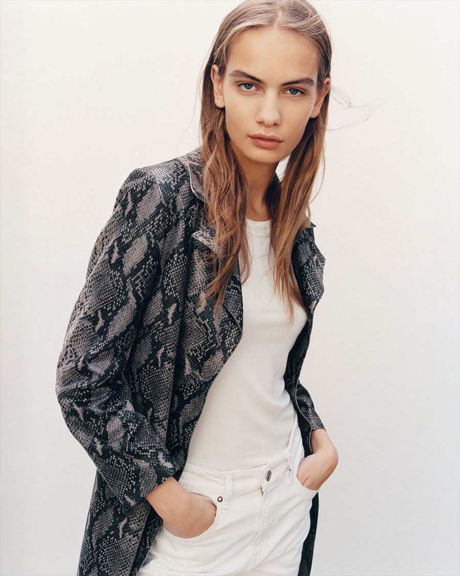 Immmagine di una donna che indossa un trench pitonato con una t-shirt bianca e un paio di jeans bianchi.