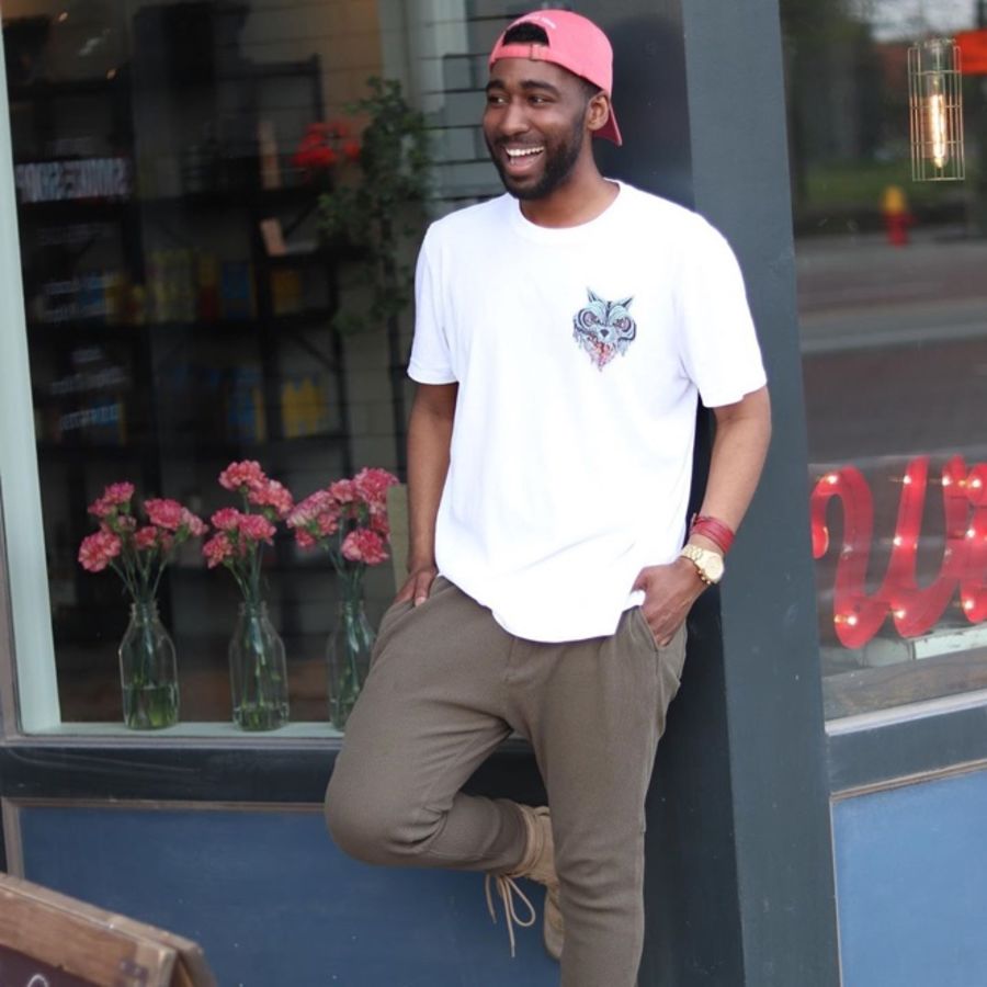 Foto von einem Mann, der ein weißes T-Shirt mit Logo und eine khakifarbene Hose trägt.
