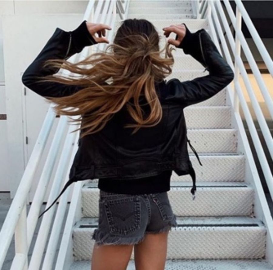 Foto von einer Frau, die auf einer Feuerleiter sitzt und eine schwarze Lederjacke und schwarze Jeans trägt.