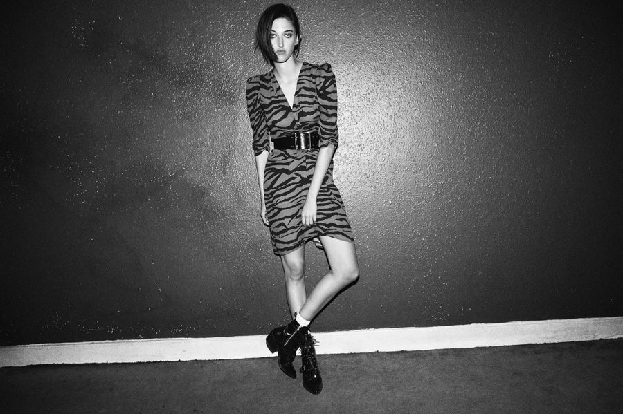 Black and white image of a woman wearing a zebra printed short dress with a leather belt and leather boots.