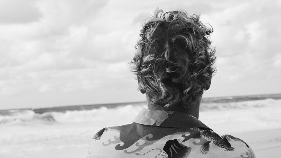 Imagen de la espalda de un hombre mirando al mar vestido con una camisa hawaiana.