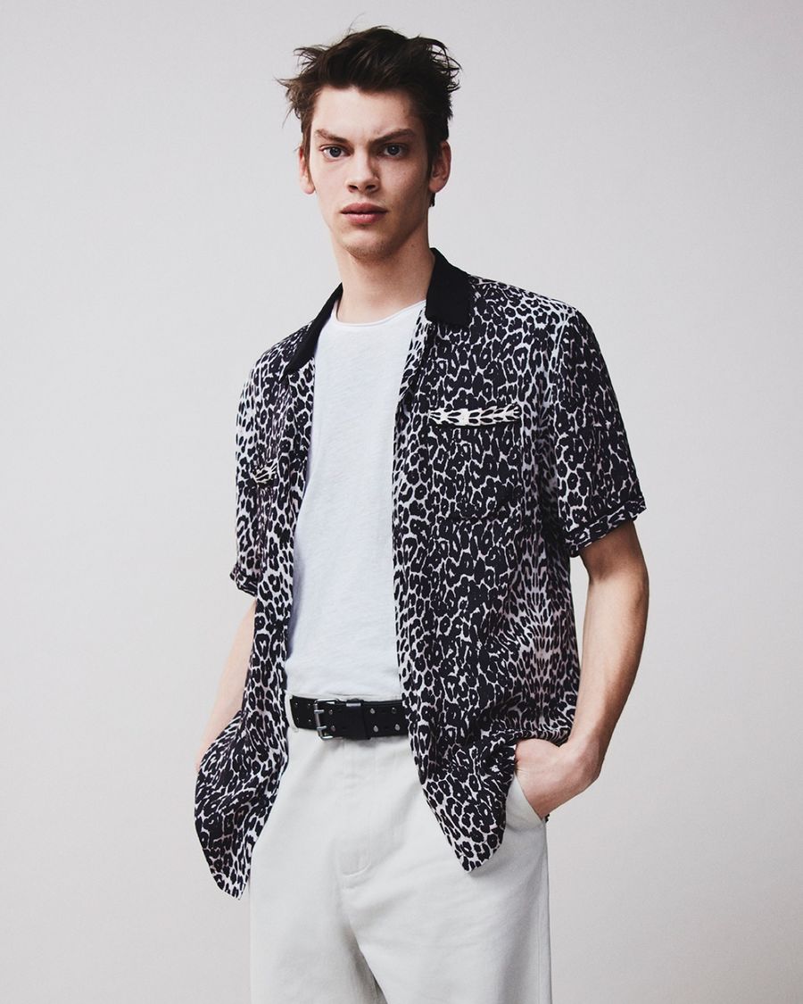 Imagen en blanco y negro de un hombre con una camisa negra con detalle bordado en el pecho.