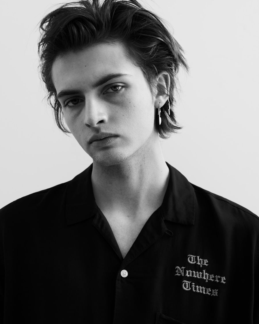 Black and white portrait of a man wearing a black shirt with an embroidery on the chest.
