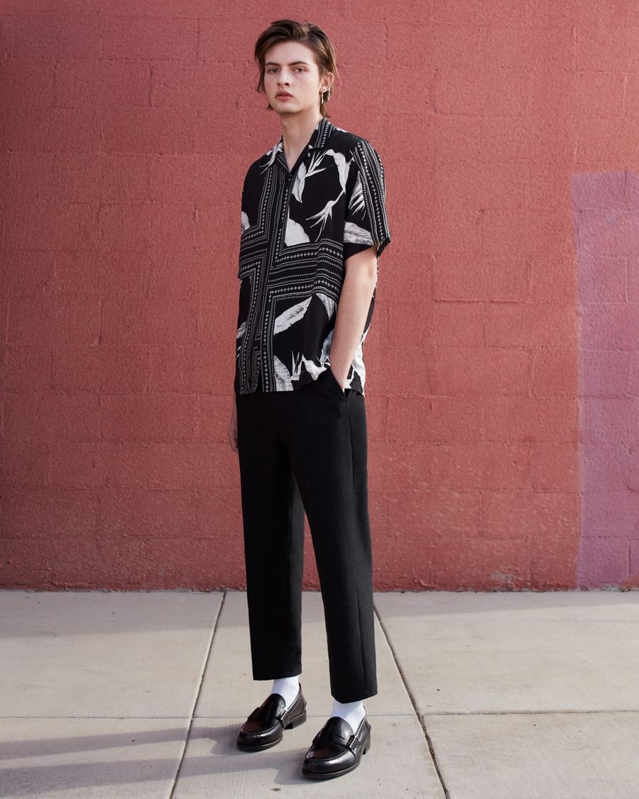 Imagen de un hombre con una camisa estampada en blanco y negro, pantalones negros y mocasines.
