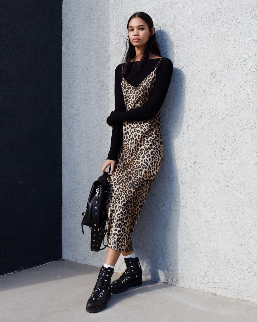 Image of a woman wearing a thin strap long leopard print dress over a black long sleeve t-shirt, black leather backpack and leather boots.