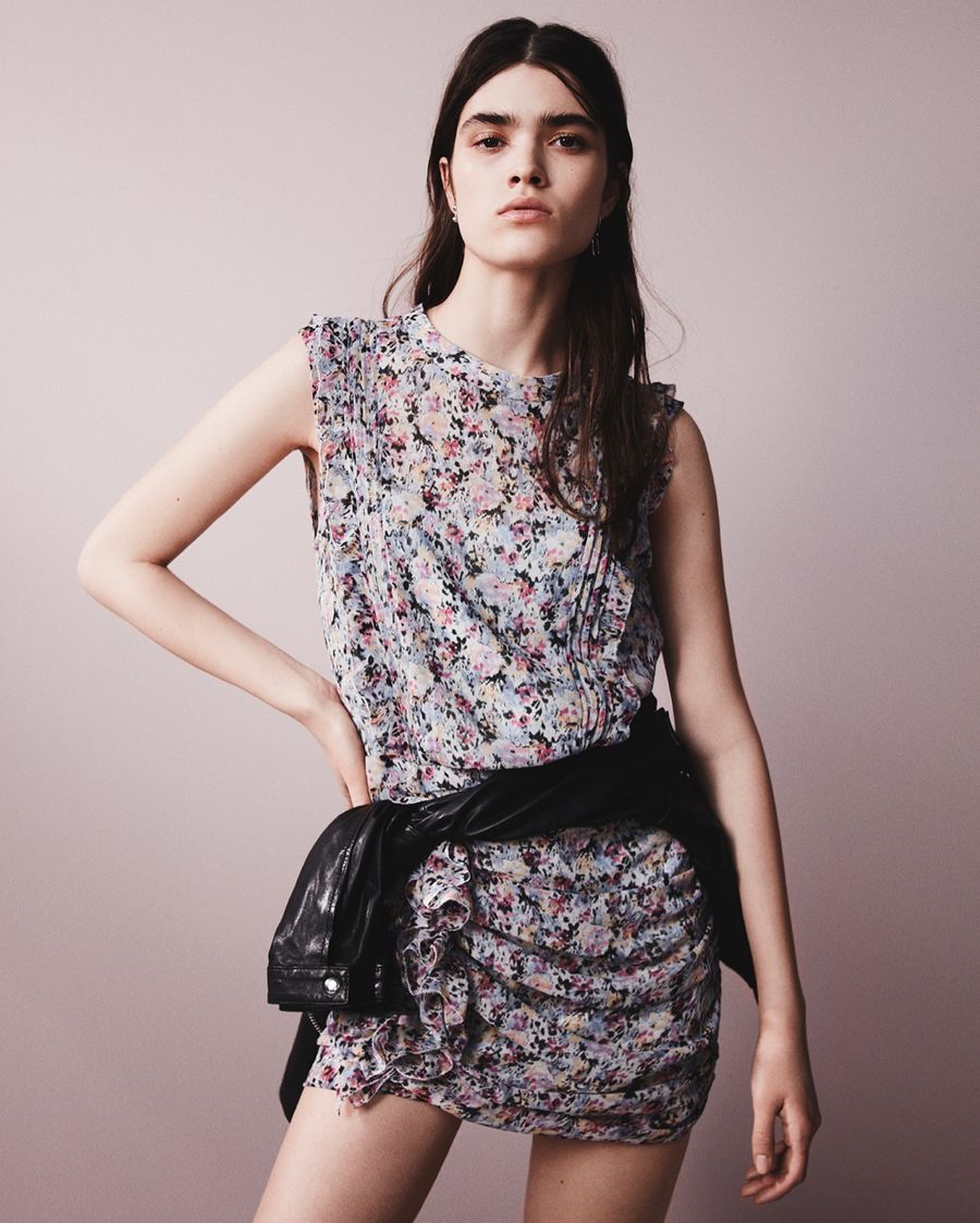 Image of a woman posing in front of a pink wall in the street and wearing a black cotton skirt with a leopard tied up shirt, dark leather jacket and black leather studded shoes.