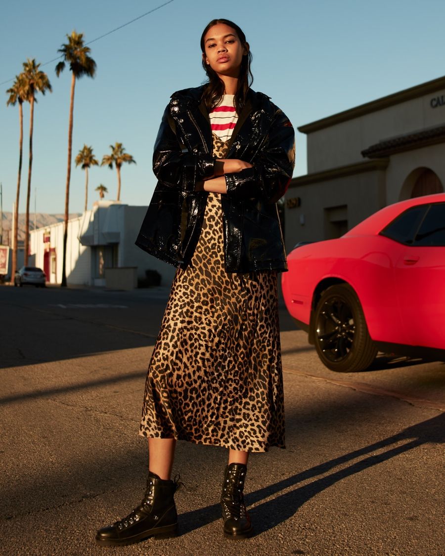 Image of a woman standing in a street in LA wearing a long leopard print silk dress over a white and red striped t-shirt and styled with a shinny black rain coat and black leather boots.