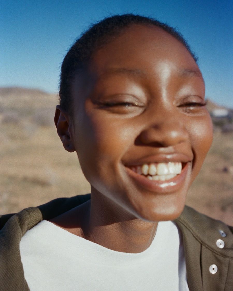 Imagen de una mujer sonriendo a la cámara con una playera blanca y una chamarra color caqui.