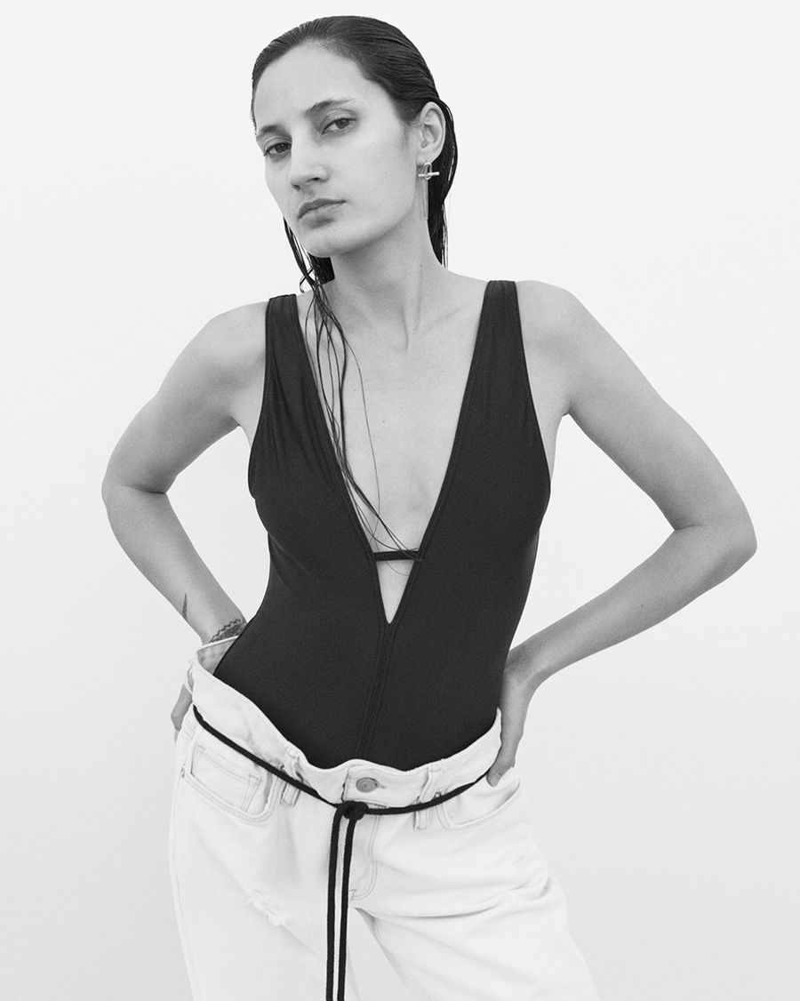 Black and white image of a woman wearing white boyfriend jeans with a black swimsuit.