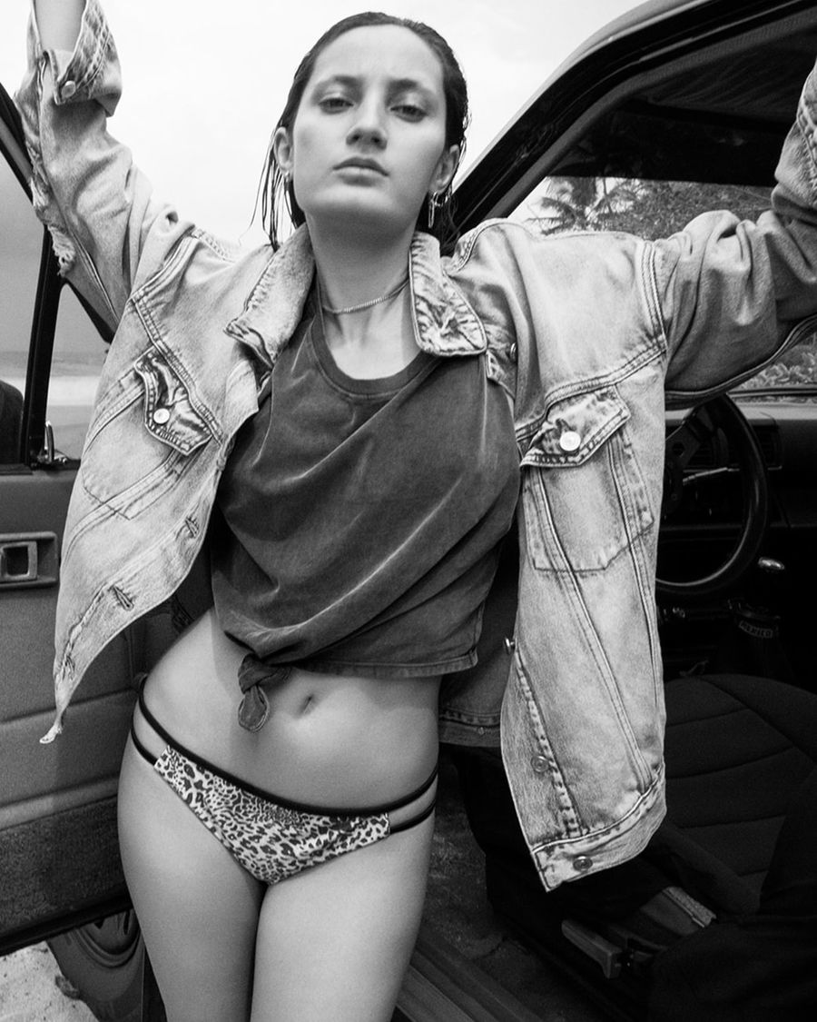 Black and white image of a woman wearing a leopard printed bikini bottoms with a black t-shirt and oversized denim jacket.