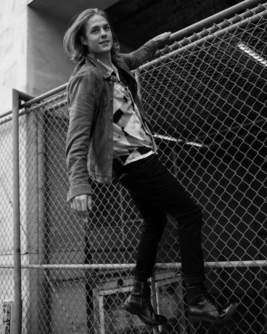 Black and white picture of Corey harper climbing a wire fence and wearing pieces from our last collection.