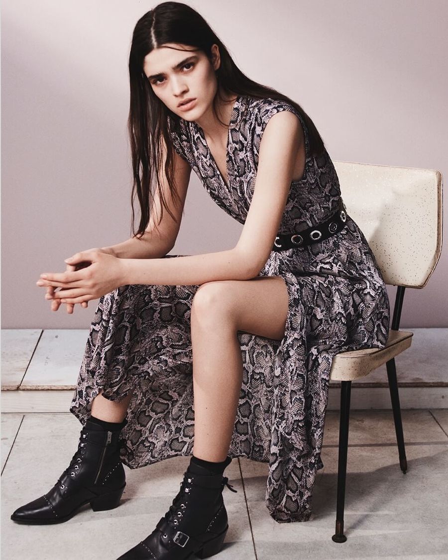 Image of a woman sitting on a chair wearing a long leopard printed dress with black studded leather boots and a black leather belt.