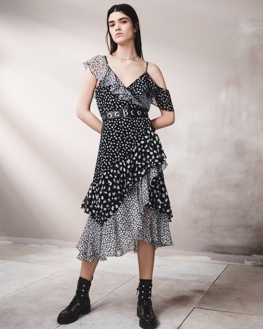 Immagine in bianco e nero di una donna che indossa un abito asimmetrico con fantasia floreale e un paio di stivaletti neri in pelle..