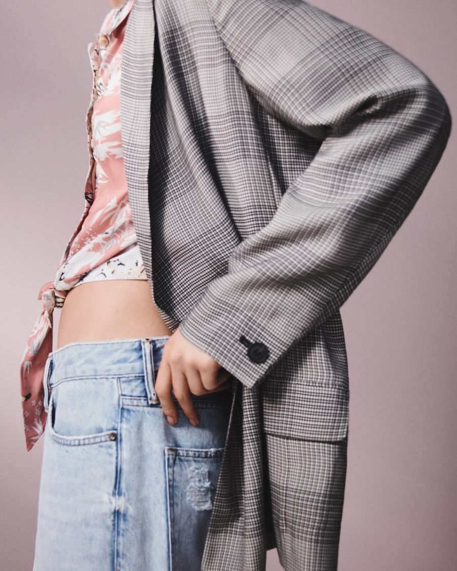 Inquadratura su una donna che indossa una camicia rosa hawaiana con un blazer a scacchi e un paio di jeans boyfriend.