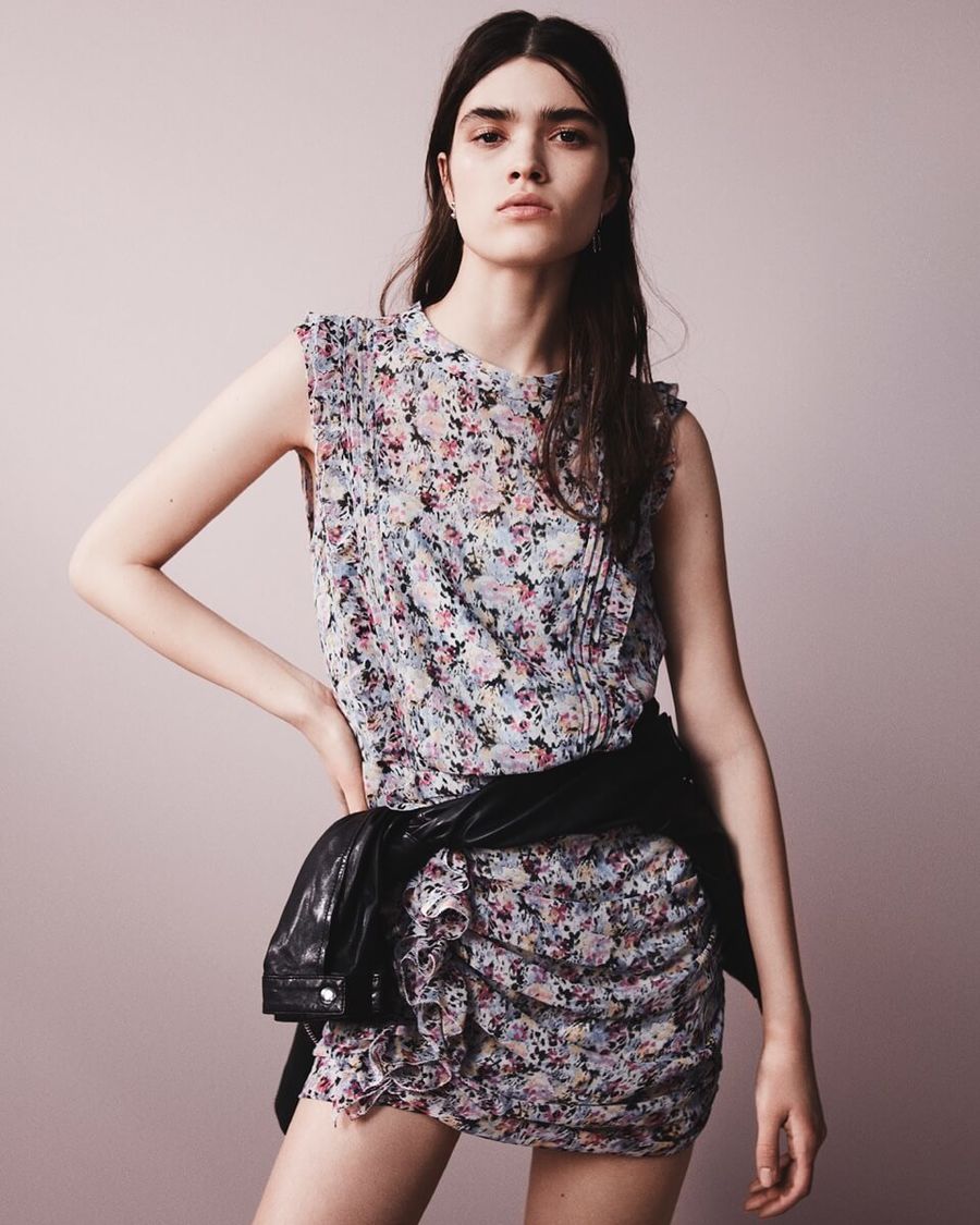Image of a woman wearing a short flower printed dress with a black leather jacket tied at the waist.