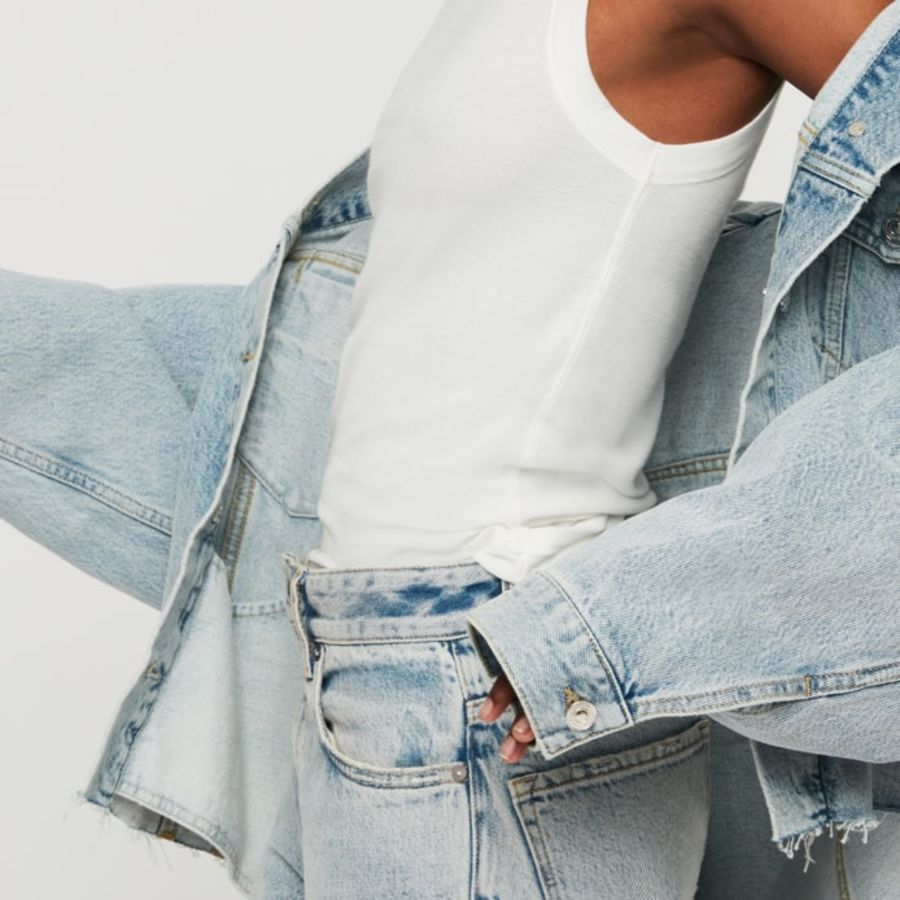 Nahaufnahme von einer Frau, die ein weißes Tanktop, helle Jeans und eine dazu passende Jeansjacke trägt.
